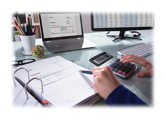 osoba liczy coś na kalkulatorze na biurku stoi laptop i leżą dokumenty
